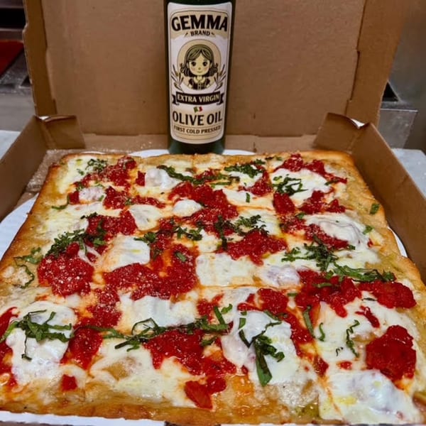 A rectangular Franco's pizza with red sauce, white cheese, and basil, with a bottle of olive oil.