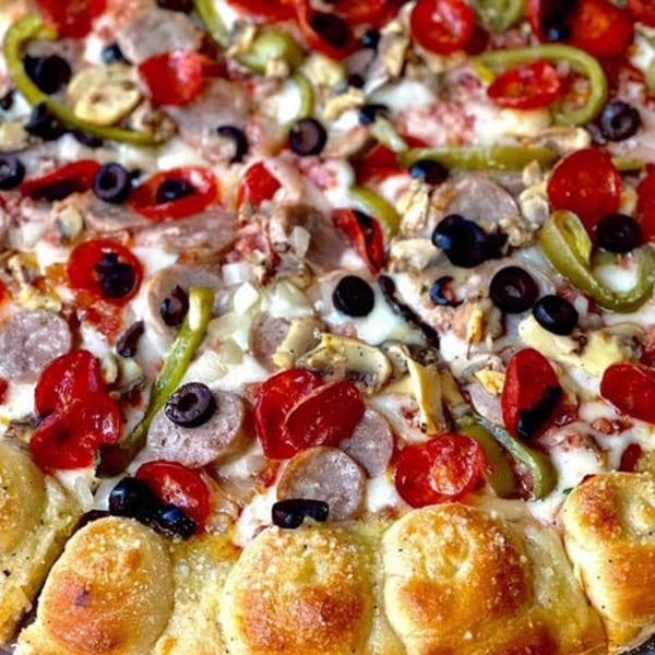 Close-up of a Franco's Italian pizza, topped with sausage, pepperoni, olives, peppers, and tomatoes.