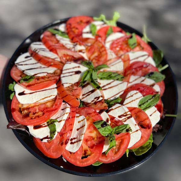 Franco's Caprese salad with sliced tomatoes, mozzarella, basil, and balsamic glaze on a black plate.
