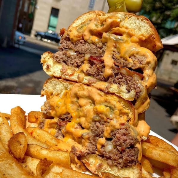 A towering double cheeseburger with melted cheese and sauce, served with a side of golden fries.